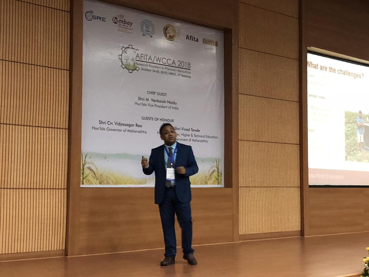 Speaker in a suit on stage in front of an AFITA/WCCA 2018 banner, with a slide reading "What are the challenges?".