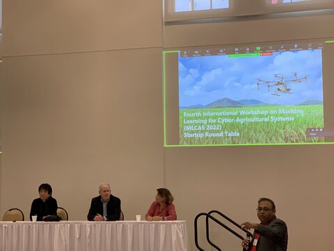 Three panelists seated at a table with a moderator standing beside a screen reading "MLCAS 2022 Startup Round Table".