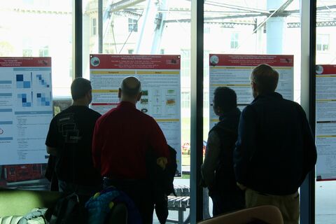 Four attendees viewing research posters mounted along a window wall.