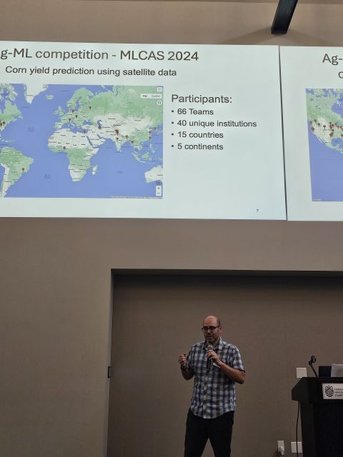 Speaker with a microphone below a slide showing a world map of competition participants.