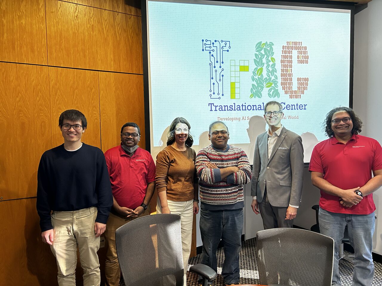 Six people standing in front of a projection screen showing the Translational AI Center logo.