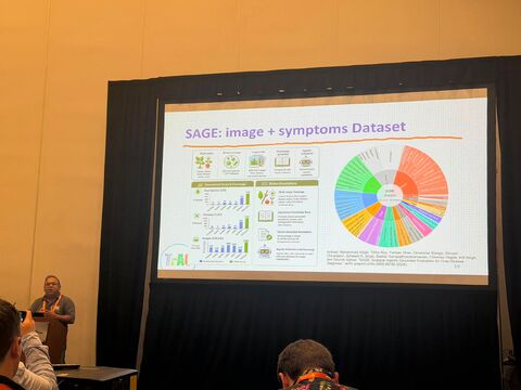 Speaker at a podium beside a projected slide titled "SAGE: image + symptoms Dataset".