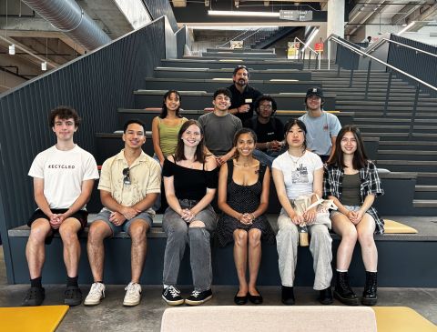 Group of thirteen people seated on wide indoor stairs in a modern building.