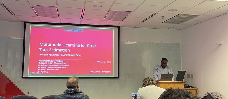 A presenter at a lectern beside a projected title slide reading "Multimodal Learning for Crop Trait Estimation".