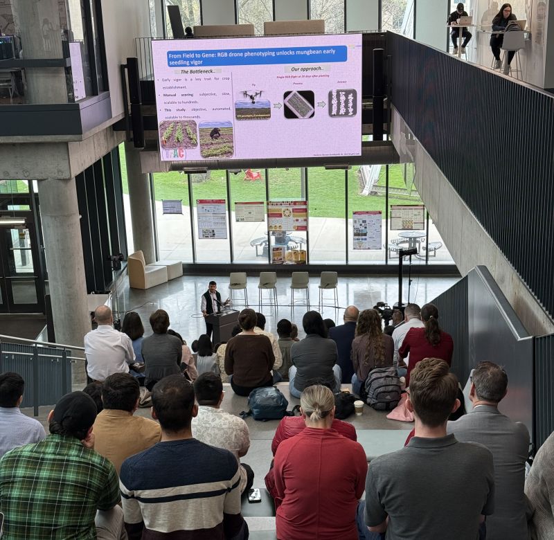 An audience seated on wide atrium steps watching a speaker at a podium below a large projected slide.