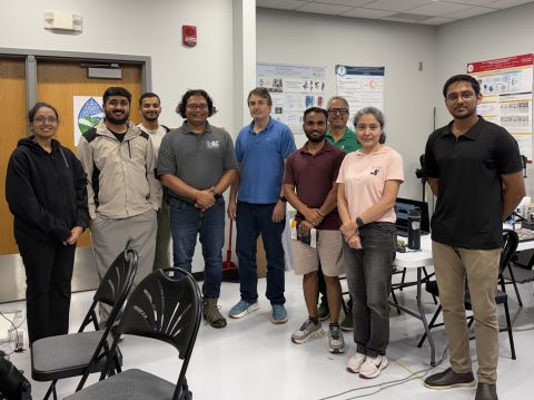 Ten people posing for a group photo in a lab room with research posters on the walls.