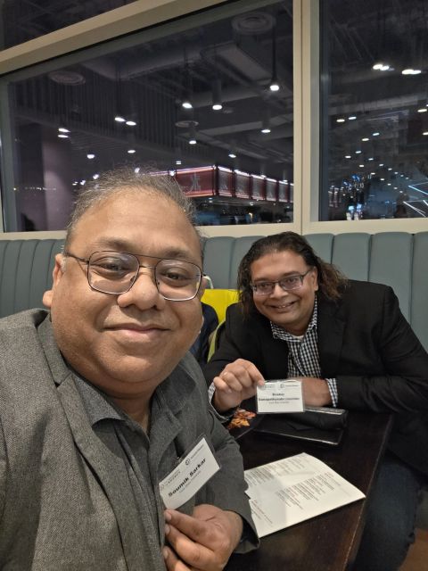 Two attendees at a table holding up their Genesis Mission Summit name badges.